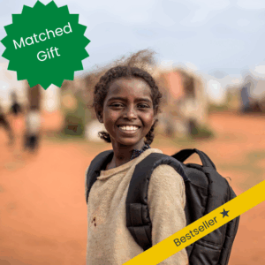 A girl from Sudan in a backpack smiles as she goes to school