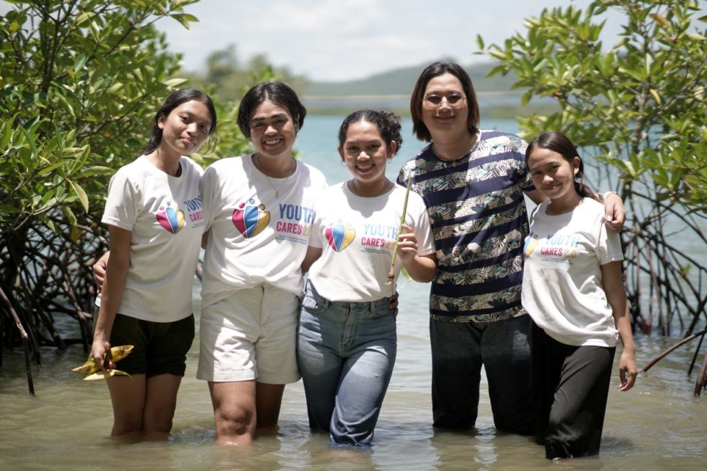 Group of friends smiling by a mangrove, participating in a youth environmental care event.