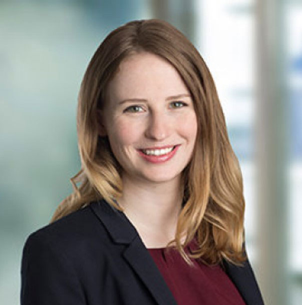 Smiling woman in a business suit with long hair, standing against a blurred office background.