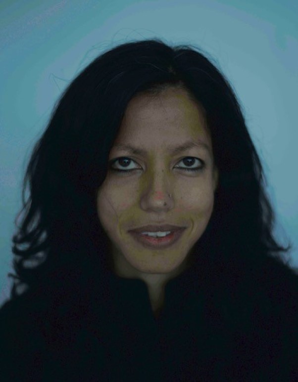 Portrait of a person with long dark hair against a blue background, looking directly at the camera with a slight smile.