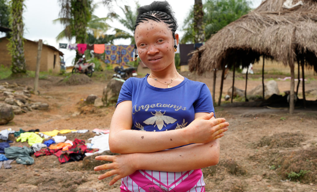A girl stands with her arms in an equal sign and smiles at the camera