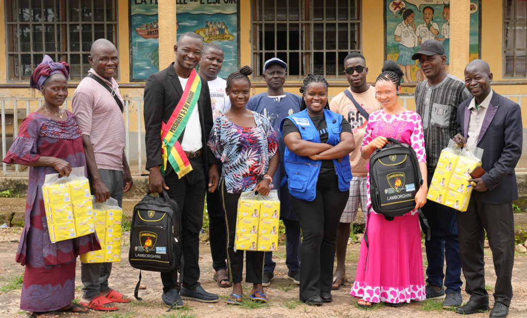 A group of people stand together - two girls receive menstrual and education supplies from school and community leaders.